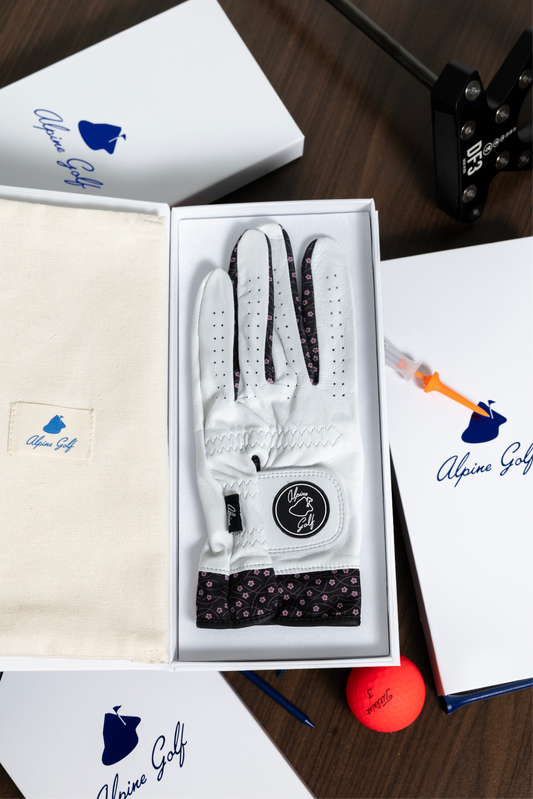 Close-up of the Alpine Golf Hana Edition glove and luxury packaging, emphasizing the texture of the white AAA Cabretta leather, the navy Japanese wave design on the cuff, and the branded magnetic box.