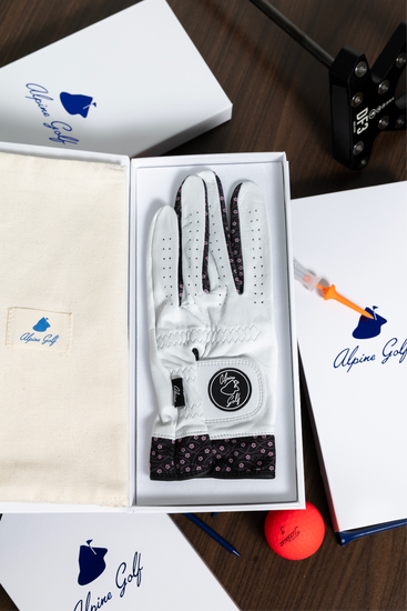 Close-up of the Alpine Golf Hana Edition glove and luxury packaging, emphasizing the texture of the white AAA Cabretta leather, the navy Japanese wave design on the cuff, and the branded magnetic box.